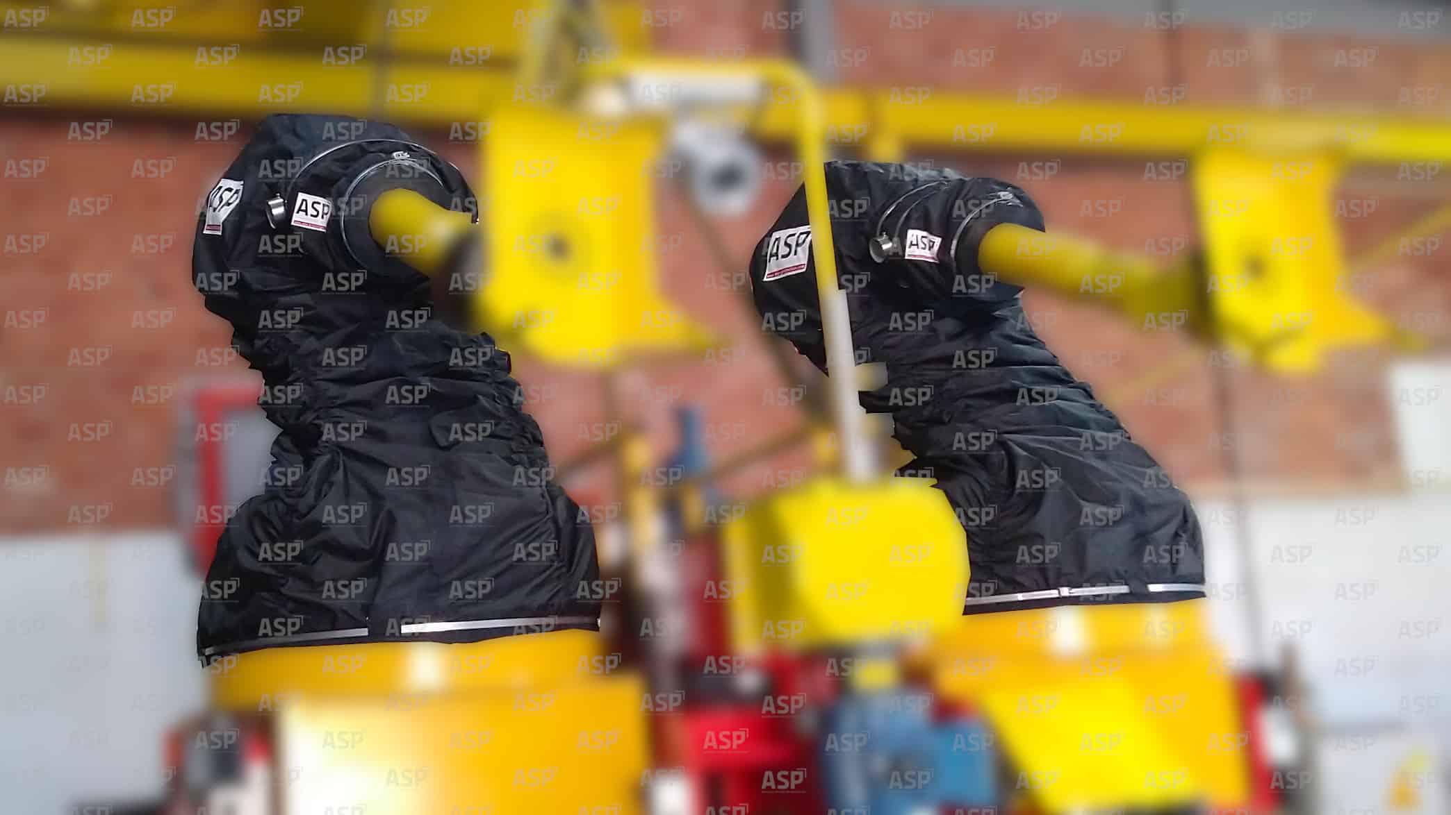 Na tejto fotografii sú dva priemyselné roboty Fanuc, všetky žltej farby, chránené dvoma čiernymi krytmi ATEX pre výbušné prostredie.